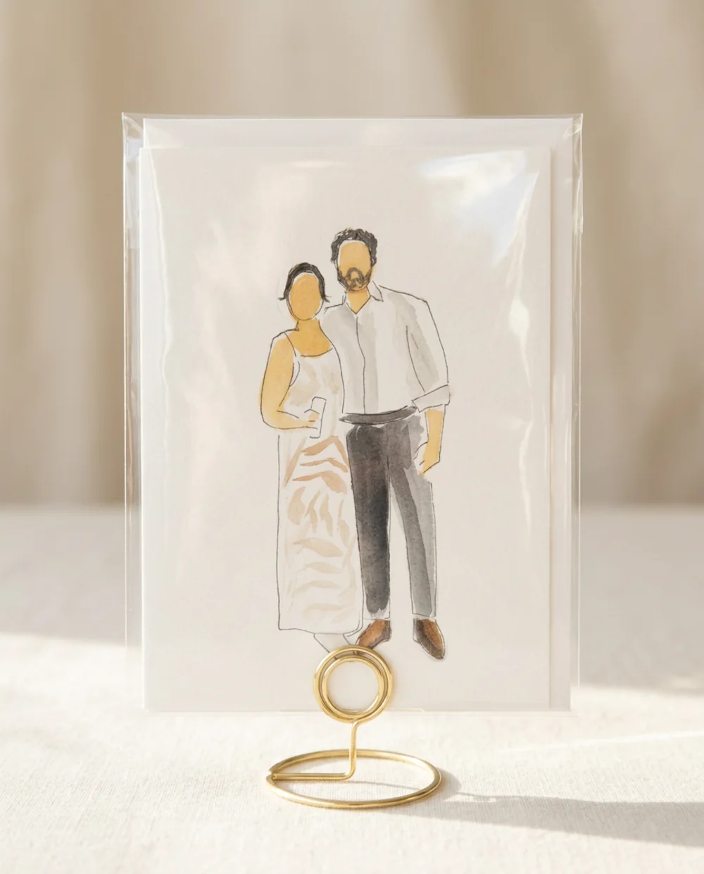Watercolour illustration of a couple in a white shirt and patterned white dress, inside a clear protective sleeve on a gold wire table stand