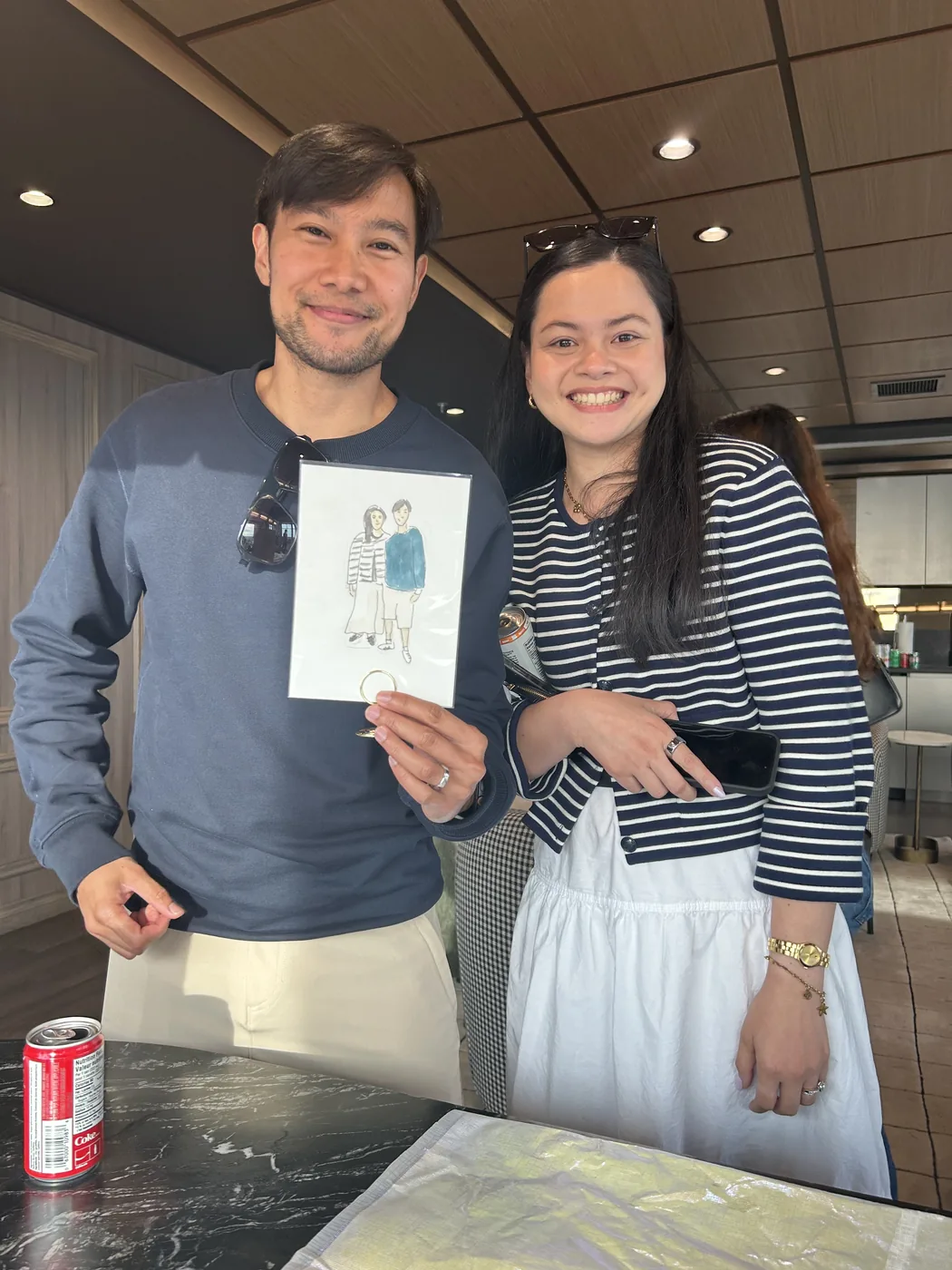 A couple holding up the ink and watercolour illustration drawn of them at a corporate event