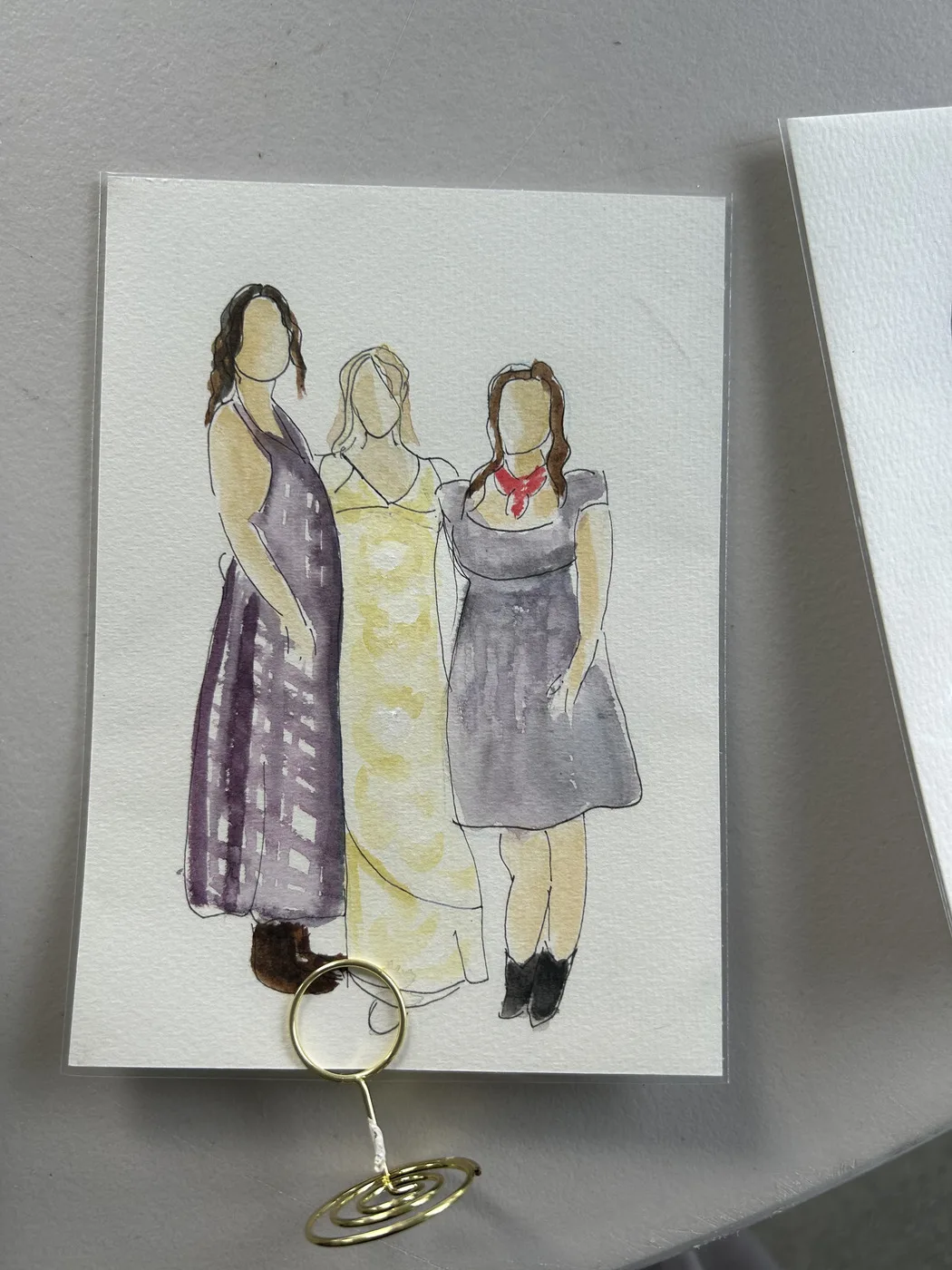 Watercolour and ink illustration of those three women, displayed in a gold table stand