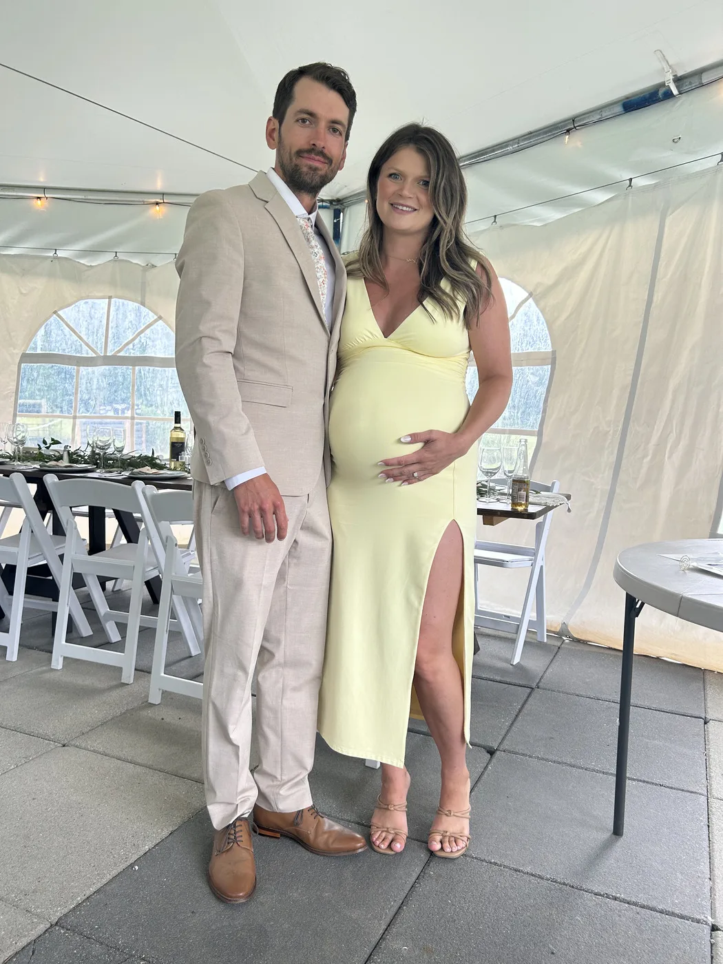 Guest photo of a man in a tan suit beside a pregnant woman in a yellow gown at a wedding reception under a white tent