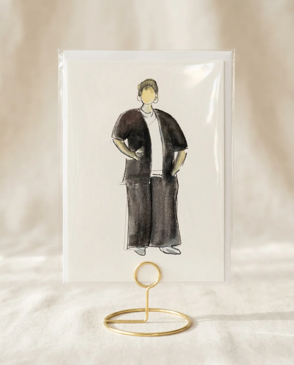Watercolour guest illustration of a woman in a black outfit, inside a clear protective sleeve on a gold wire table stand