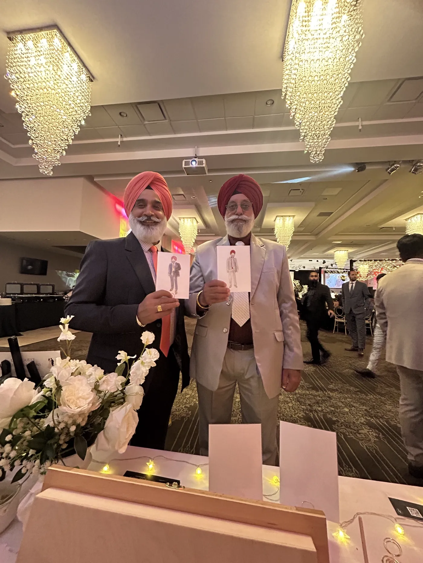 Two guests in turbans holding the watercolour illustrations painted of them at the same banquet reception