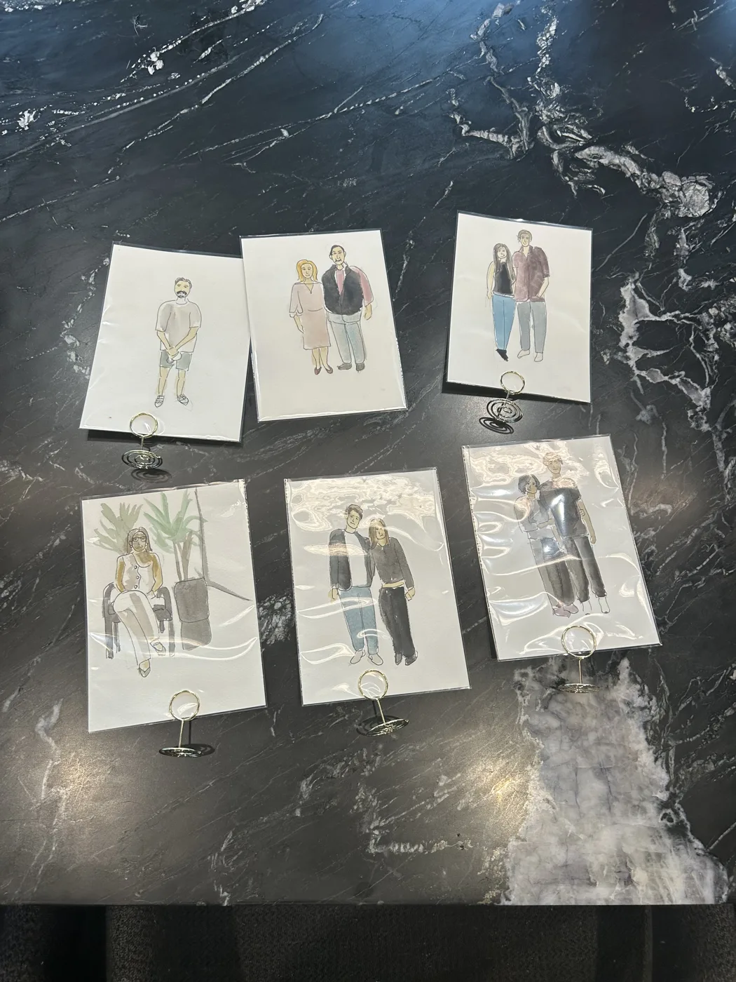 Six finished guest illustrations laid out on a dark marble table