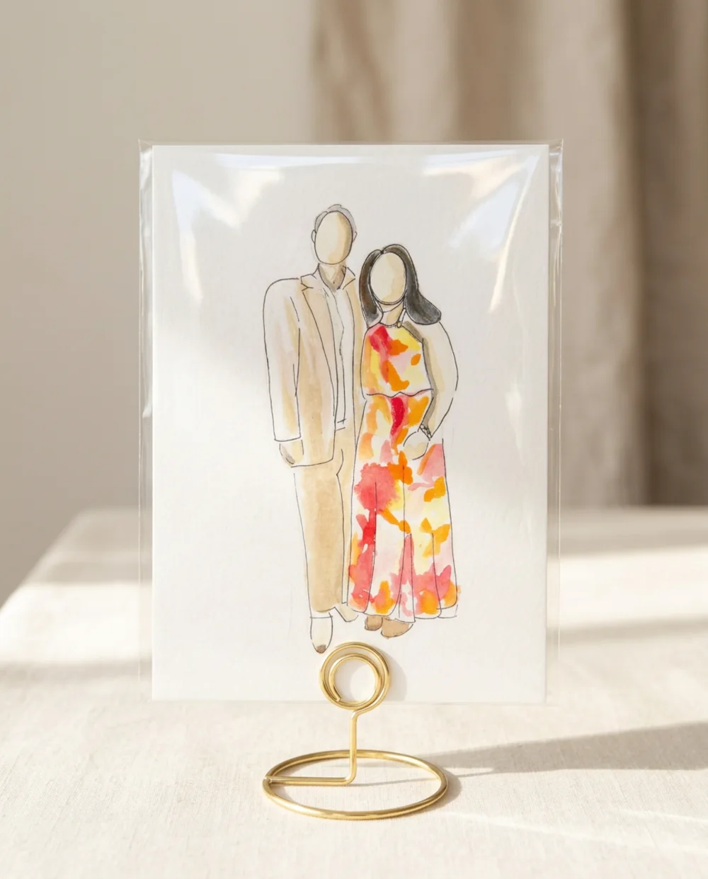 Watercolour illustration of a couple in a tan suit and colourful floral dress, inside a clear protective sleeve on a gold wire table stand