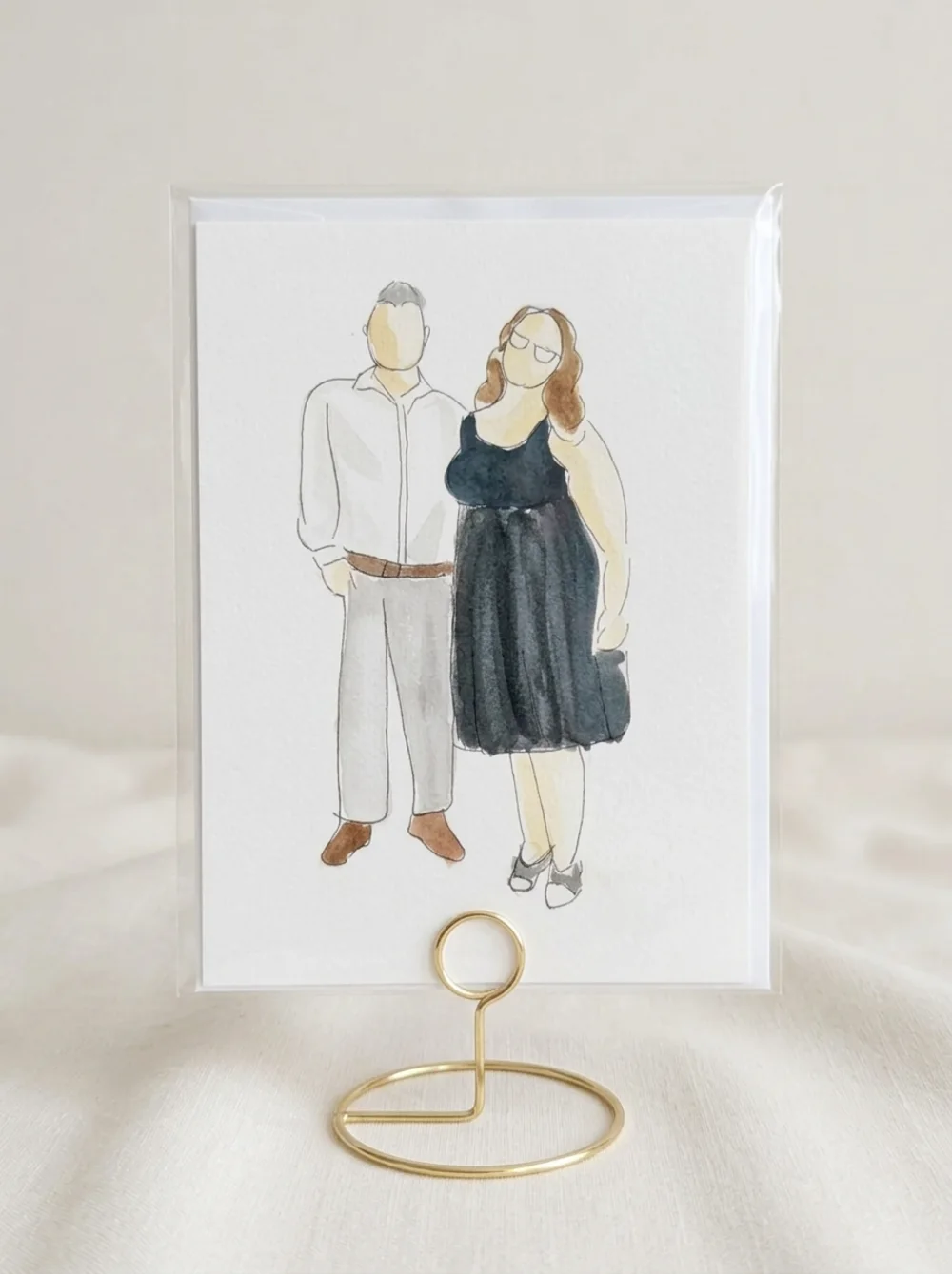 Watercolour and ink illustration of a couple, the man in a white shirt and the woman in a dark dress and glasses, inside a clear protective sleeve on a gold wire table stand