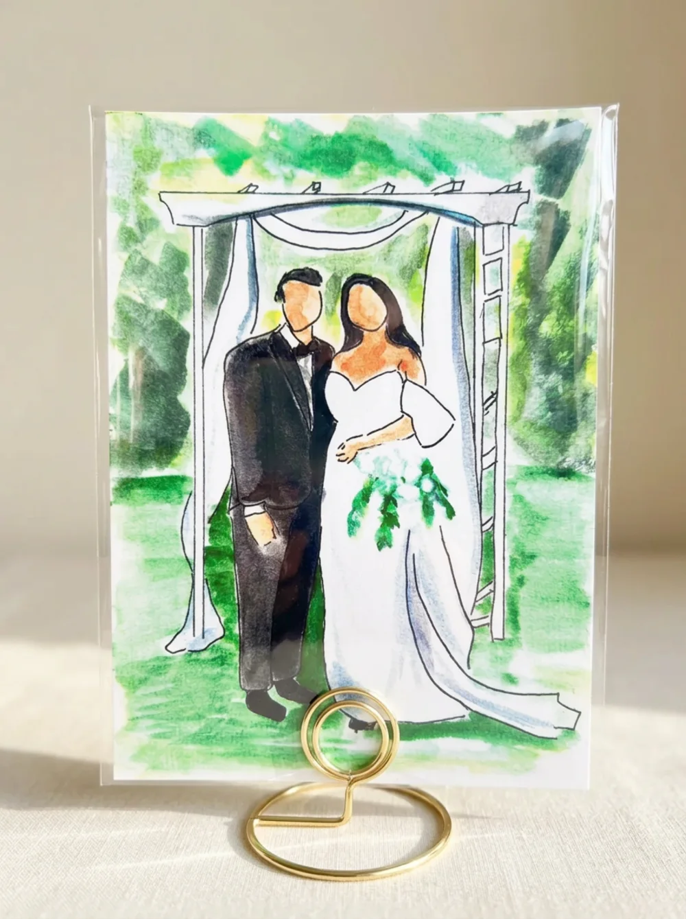 Loose watercolour illustration of a bride and groom beneath a white ceremony arch on a green garden wash, inside a clear protective sleeve on a gold wire table stand